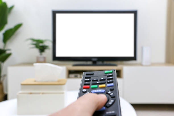 istock Streaming and watching TV, movie night, first-person view, pressing remote control, white blank TV screen blurred in background. Clean and modern living room interior. 1623205803
