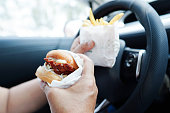 Asian woman driver hold and eat hamburger and french fries in car, dangerous and risk an accident.