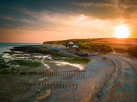Aerial view, taken by drone, depicting the majestic Seven Sisters cliffs beyond and Cuckmere Haven beach in the south of England, UK. It is sunset and the beautiful scenery is bathed in golden light.