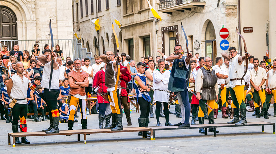 Gualdo Tadino, Umbria, Italy, August 17 -- Some archers compete during the traditional medieval games in the town of Gualdo Tadino, in Umbria, central Italy. Some archers compete during medieval games in the heart of the medieval town of Gualdo Tadino, in Umbria, central Italy. The archers dressed in traditional medieval clothes represent the different districts of the town. The Umbria region, considered the green lung of Italy for its wooded mountains, is characterized by a perfect integration between nature and the presence of man, in a context of environmental sustainability and healthy life. In addition to its immense artistic and historical heritage, Umbria is famous for its food and wine production and for the high quality of the olive oil produced in these lands. Image in 16:9 ratio and high definition quality.