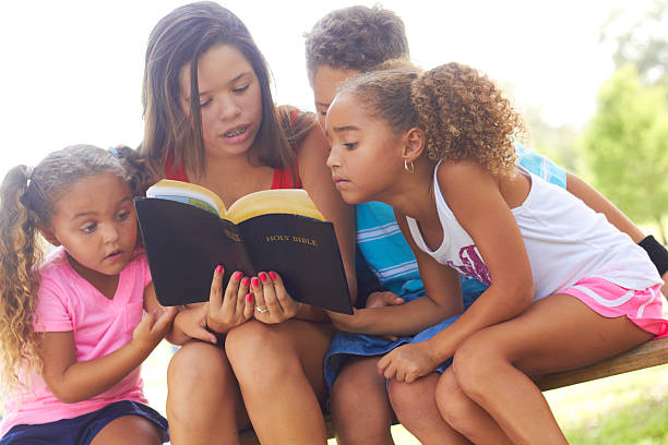 teenager mädchen lesen bibel zu geschwistern im park - bible holding reading book stock-fotos und bilder