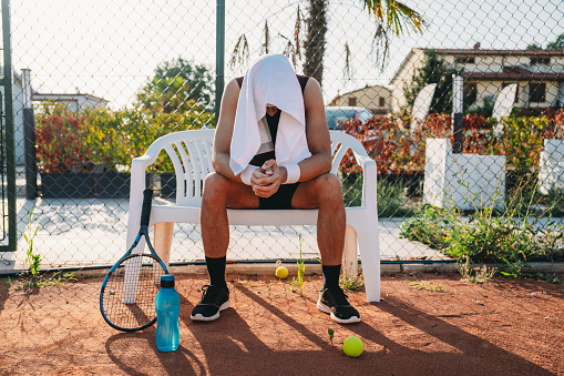 A tennis player is resting during a match. He has a towel on his head.