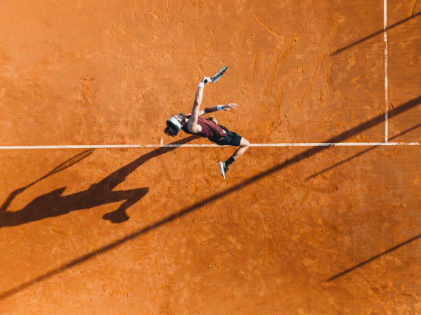 Aerial view of a tennis player during a match Aerial view of a tennis player during a match. Drone shot directly from above. Orange tennis court field. tennis stock pictures, royalty-free photos & images