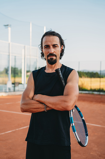 Portrait of tennis player holding his racket. He's standing on the clay court.