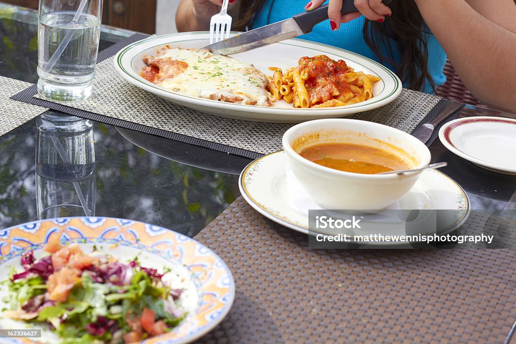 Mulher comendo frango com parmesão com sopa e salada em primeiro plano - Foto de stock de 20 Anos royalty-free