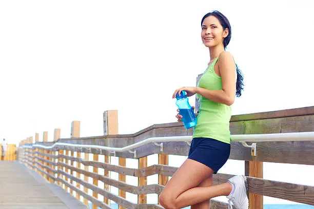 Healthy young woman holding waterbottle on boardwalk.