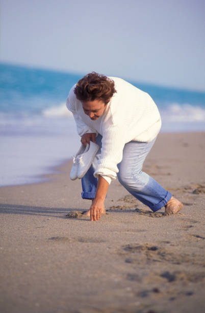 istock Senior woman picking up seashells on the beach 1623317467