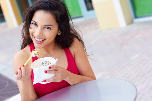 Portrait of a happy young woman enjoying frozen yogurt at cafe table. Horizontal shot.