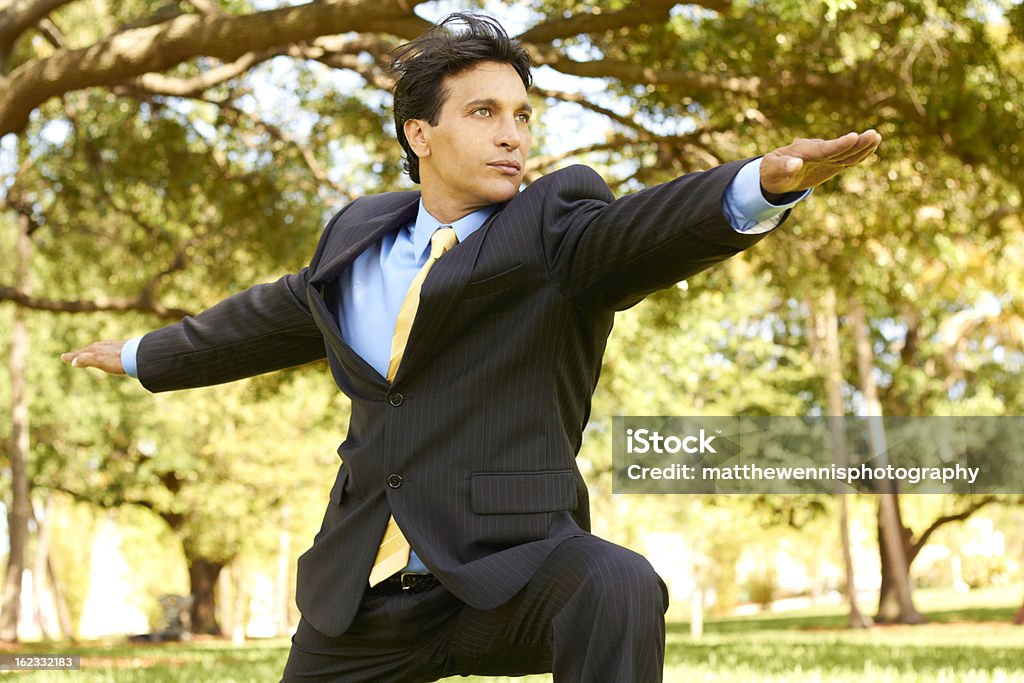 Ispanico Uomo d'affari facendo Posa del guerriero Yoga al parco - Foto stock royalty-free di Completo