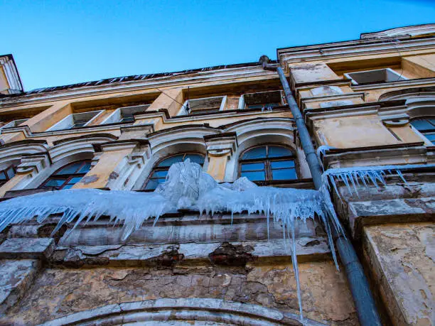 Photo of an old dilapidated Baroque building in the city. A dilapidated building with icicles and cracks.