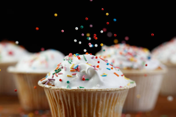 Сupcakes or muffins decorated with confectionery decor on a wooden background. Сonfectionery confetti, balls flying in the air. Shallow depth of field
