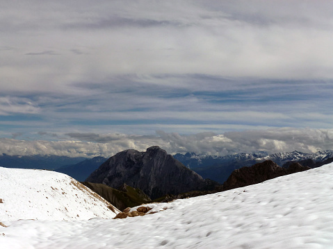 A view from a snow-covered mountain peak to a nearby mountain. Above her is a cloudy sky. The mountain ranges of other mountains are in the distance
