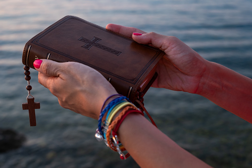 Woman wearing LGBT rainbow bracelet with Holy Bible at sunset