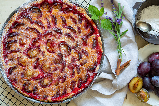 Homemade pie with plums and sieve on the table.
