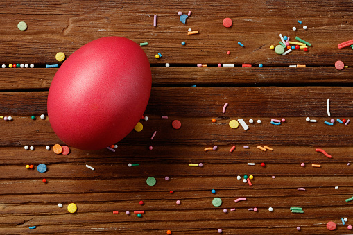Easter egg and confectionery decor is scattered on a wooden table. Festive background. Confectionery confetti, balls lie on a wooden background. Directly above