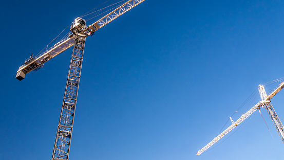 Two white construction cranes against a deep blue sky