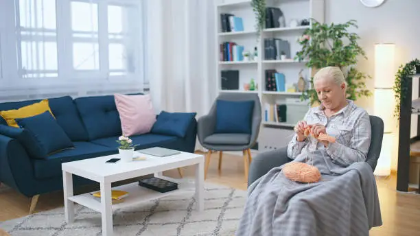 A mature woman is sitting in an armchair, knitting and enjoying her favorite hobby