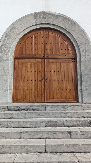 A large wide door made of boards, the entrance to the church, a wide staircase made of stone and a white wall photo