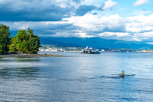 Vancouver, British Columbia - July 25, 2023: The view of Coal Harbour seaside park, a woman is playing a canoe on the water, Vancouver, Canada.