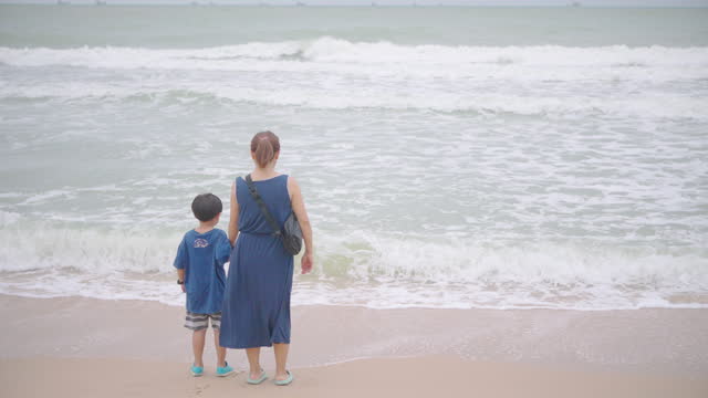 Asian mother is walking and having fun with her little boy on the sandy beach.