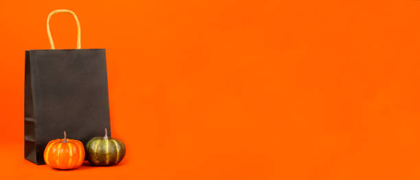 istock Halloween. Black paper package, pumpkins stand next to an orange background. 1623461064
