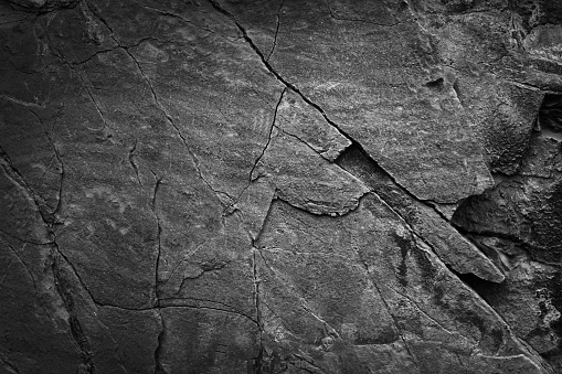 Black white dark gray grunge background. Stone rock texture. Rough mountain surface. Close-up. It looks like a concrete wall of a house. Cracked broken scratched old damaged dirty. For design.