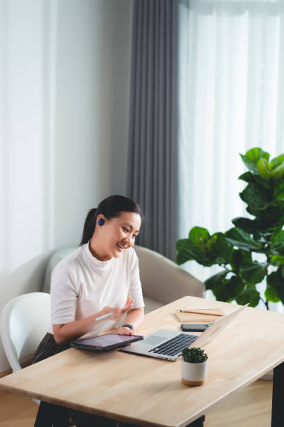 istock Asian woman enjoy with working online, reading data on tablet and using laptop talking on video conference, sitting at home office. 1623490696