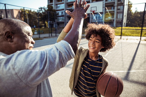 Close up of a Grandfather and grandson high fiving while playing basketball together on an outdoors basketball court
