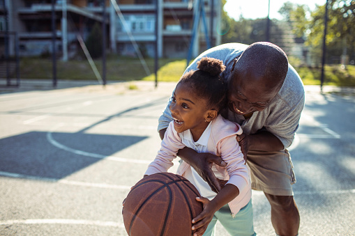 Close up of a Grandfather and granddaughter playing basketball together on an outdoors basketball court