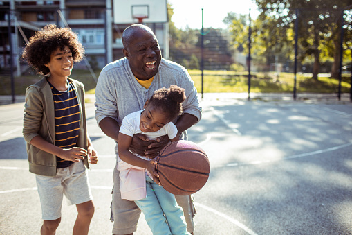 Close up of a Grandfather playing basketball with his grandchildren on an outdoors basketball court