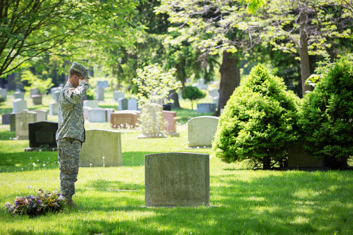 American vet saluting at a grave in a cemetery to pay respect.