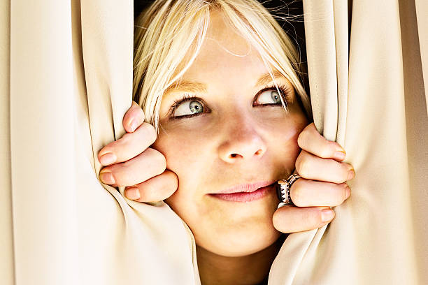 istock Cute blonde peeping sideways through curtains, smiling shyly 162355805
