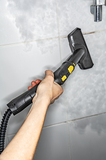 Woman washing ceramic tiles in the bathroom with a steam generator, home cleaning concept