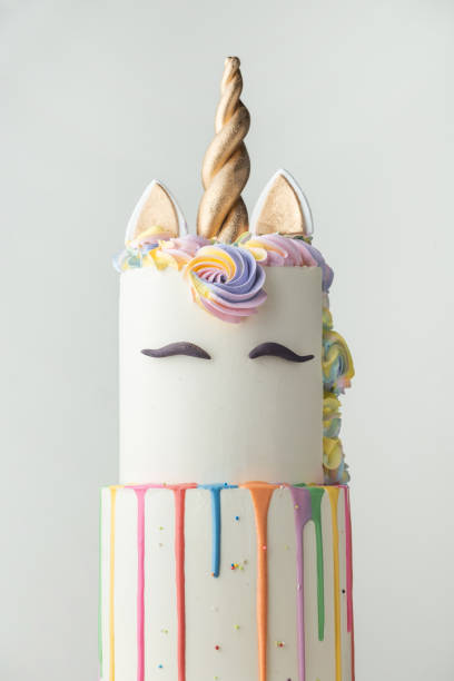 istock Big bunk cake with white chocolate frosting decorated with colorful drips, mastic eyebrows and golden ears with horn on top. Birthday party unicorn cake for a little girl on the white background. 1623592330