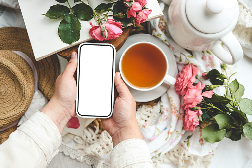 Phone in hands with an isolated screen on the background of a cup of tea.
