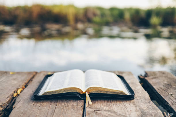 istock Open Bible on a wooden board near the river 1623667885