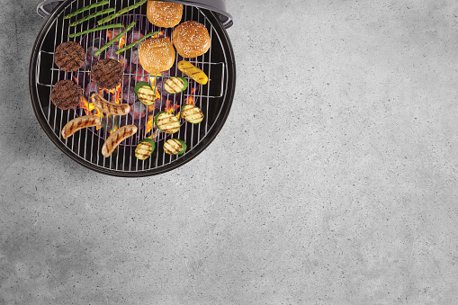 Top view of a portable bbq grill with burgers, buns, sausages & veggies