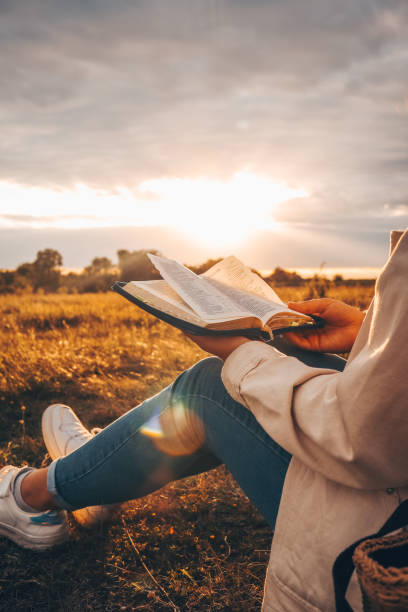 Christian woman holds bible in her hands. Reading the Holy Bible in a field during beautiful sunset. Concept for faith, spirituality and religion. Peace, hope Christian woman holds bible in her hands. Reading the Holy Bible in a field during beautiful sunset. Concept for faith, spirituality and religion. Peace, hope worshipper stock pictures, royalty-free photos & images