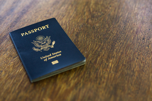 One blue American passport laying on a wooden desk