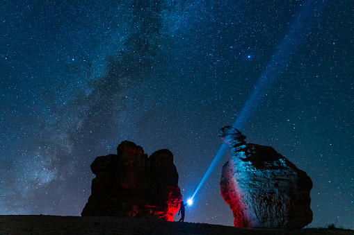 a person watching a meteor shower in the dark area with fairy chimneys. In the dark, millions of stars and the Milky Way are visible in the sky. Taken with a full-frame camera using the long exposure technique.