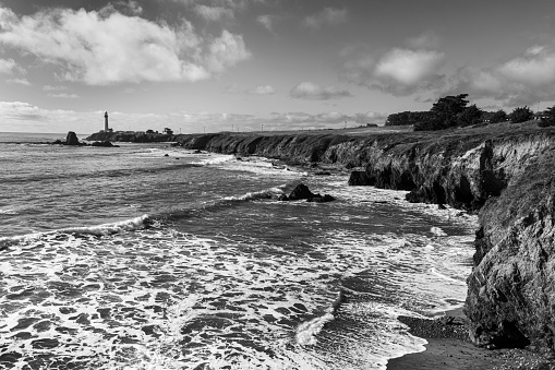 Monochrome view of Pigeon Point Lighthouse in the distance along the rocky shore of the Northern California coast.  This is the tallest lighthouse on the West Coast of the United States.

Taken from Pigeon Point Light Station State Historic Park