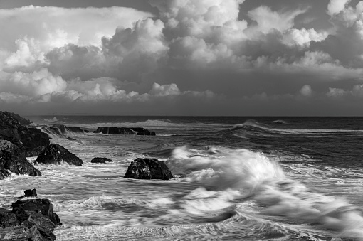 Monochrome view of turbulent ocean waves crashing on rocky shore, off the California Coast, after a pacific coast storm passed through the area.\n\nTaken at Santa Cruz, California, USA