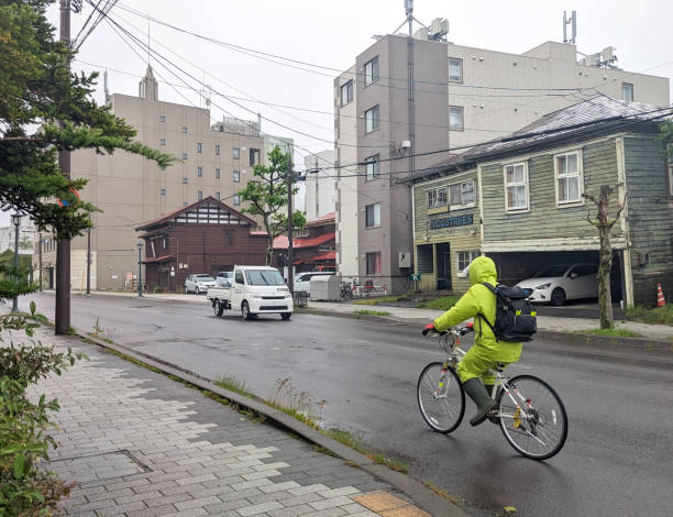 Hakodate, Japan - June 10, 2023: A cyclist in rain gear heads southeast by Hakodate Bay on a spring morning.