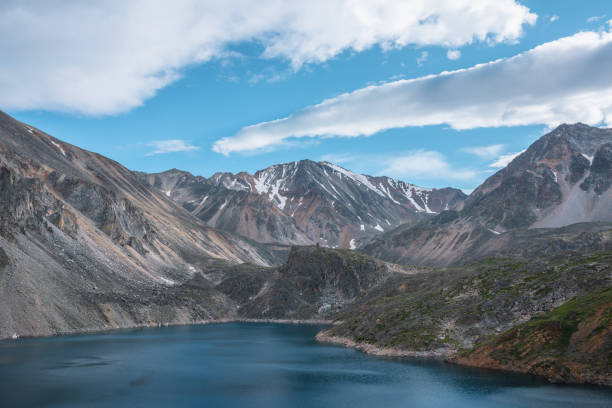 istock Deep mountain lake of phantom blue color among sharp rocks and high mountains in changeable weather. Wonderful dramatic view to deep blue mountain lake and large sunlit rocky cliff under cloudy sky. 1623995153