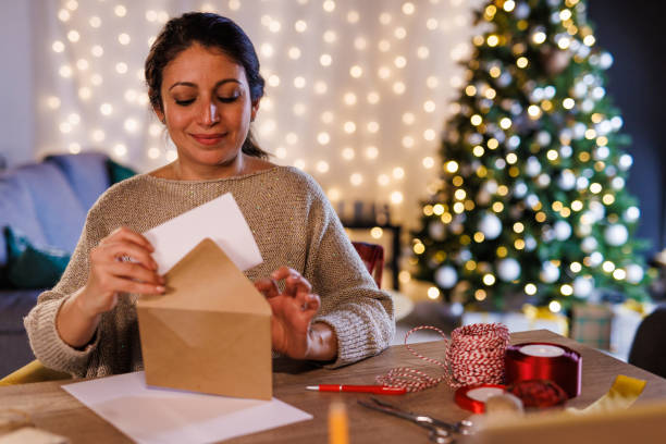 Woman putting a Christmas letter, that she wrote, in a gold colored envelope