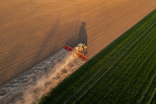 Agricultural tractor with a long trail of dust, working in field, aerial view.