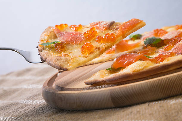 Slice of pizza with salmon and salmon caviar taken from wooden pizza peel with steel pizza slice server