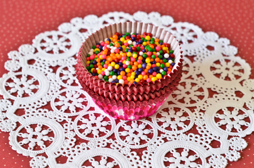 Multi colored round sprinkles in a paper cup on red background