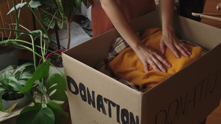 Donation concept. Hands packing clothes into donation box at home.