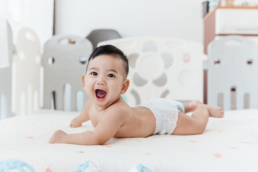 Happy Asian baby start to crawling on a bed at home, Adorable development 5 months old. Baby healthcare hygiene concept.
